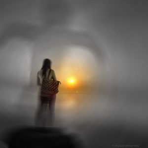 Eine Frau steht vor dem Sonnenuntergang. Das Bild wirkt düster. Vielleicht leidet diese Frau an Psychosen.r
