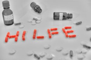 Das Wort Hilfe ist in rot zu sehen, gelegt von Tabletten. Daneben sieht man leere Fläschen und Pillen liegen in schwarz-weiß. Einige Menschen sehen nicht, dass sie an einer Cannabissucht leiden.