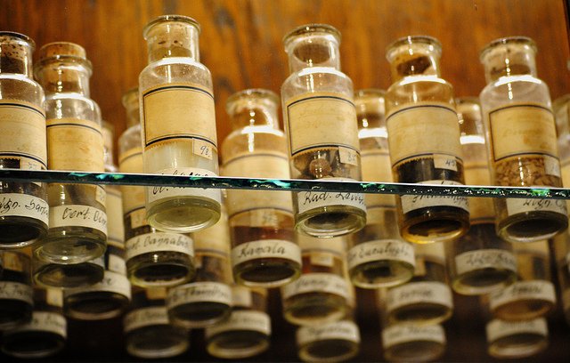 hier sind alte Apotheken Fläschen auf einem Glasregal zu sehen. In diesem Beitrag wird beschrieben, wie Cannabis zum legalen Medikament wurde.