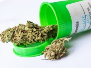 Eine grüne Medikamenten Packung liegt und Cannabisblüten sind darin. 
