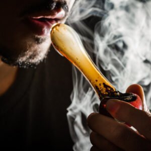 Ein Mann raucht Cannabis aus einer Pfeife und es raucht stark. 