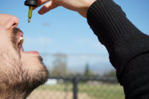 Ein Mann tropft sich mit einer Pipette eine gelbliche Flüssigkeit in den Mund, vielleicht handelt es sich dabei um die Cannabisarznei Dronabinol