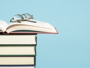 Fünf Bücher sind aufeinander gestapelt. Das oberste ist geöffnet und eine Brille liegt darauf.