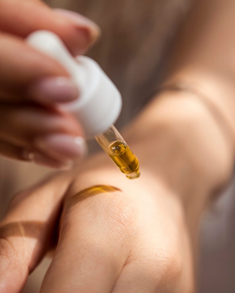 Eine Pipette mit einer bräunlichen Flüssigkeit ist zu sehen, die auf eine Hand geträufelt wird. Evtl. ein Cannabisblütenextrakt