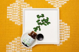 Ein Braunglas, das auf einem weißen Tablett liegt, ist umgefallen und grüne Pillen sind heraus gefallen. Sind es vielleicht Cannabis-Medikamente?