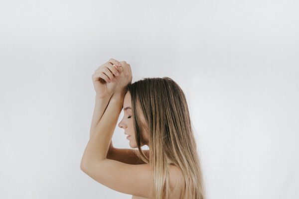 Eine junge Frau mit blonden Haaren ist im Profil zu sehen. Sie hält die Fäuste verschränkt über die Arme, man kann erkennen, dass sie atmet. Bei Asthma Erkrankungen fällt das Atmen manchmal schwer.