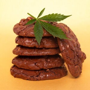 Auf dem Bild sieht man fünf aufeinander gestapelte Schokocookies. Ein Cookie lehnt an dem Stapel und darauf liegt ein Cannabisblatt.