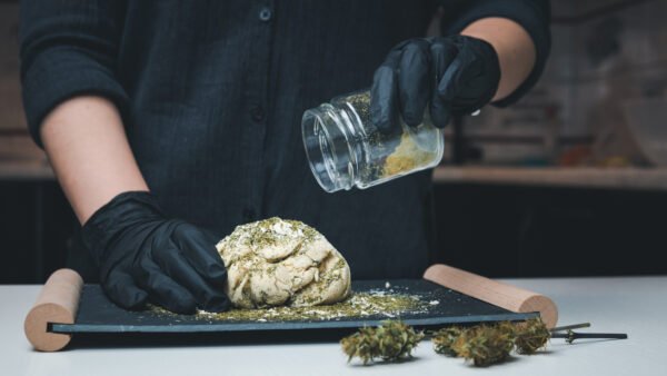 Hier sieht man eine Köchin mit schwarzen Handschuhen, die in einen Brotteig Cannabis gibt. Sie betreibt also infused Cooking.