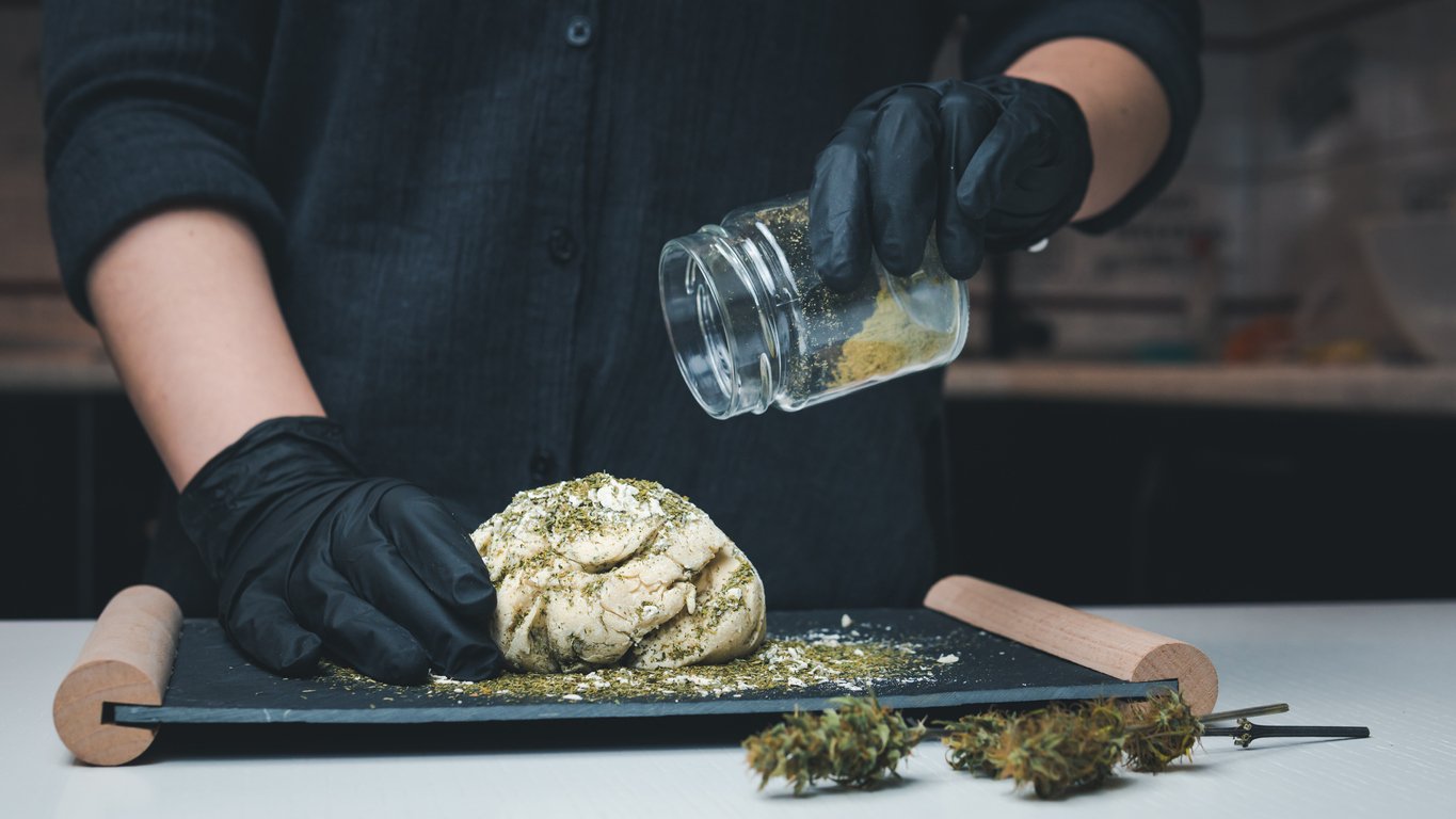 Hier sieht man eine Köchin mit schwarzen Handschuhen, die in einen Brotteig Cannabis gibt. Sie betreibt also infused Cooking.