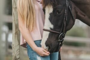 CBD für Tieren- hier sieht man ein Mädchen mit blonden langen Haaren, das liebevoll ihr Pferd streichelt. 