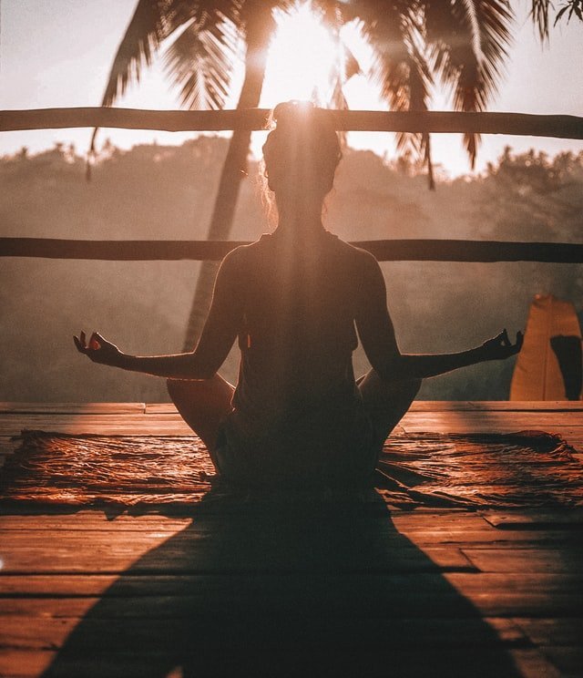 Eine meditierende Frau ist hier vor einem Sonnenuntergang zu sehen. Ob sie wohl CBD und Yoga kombiniert hat?