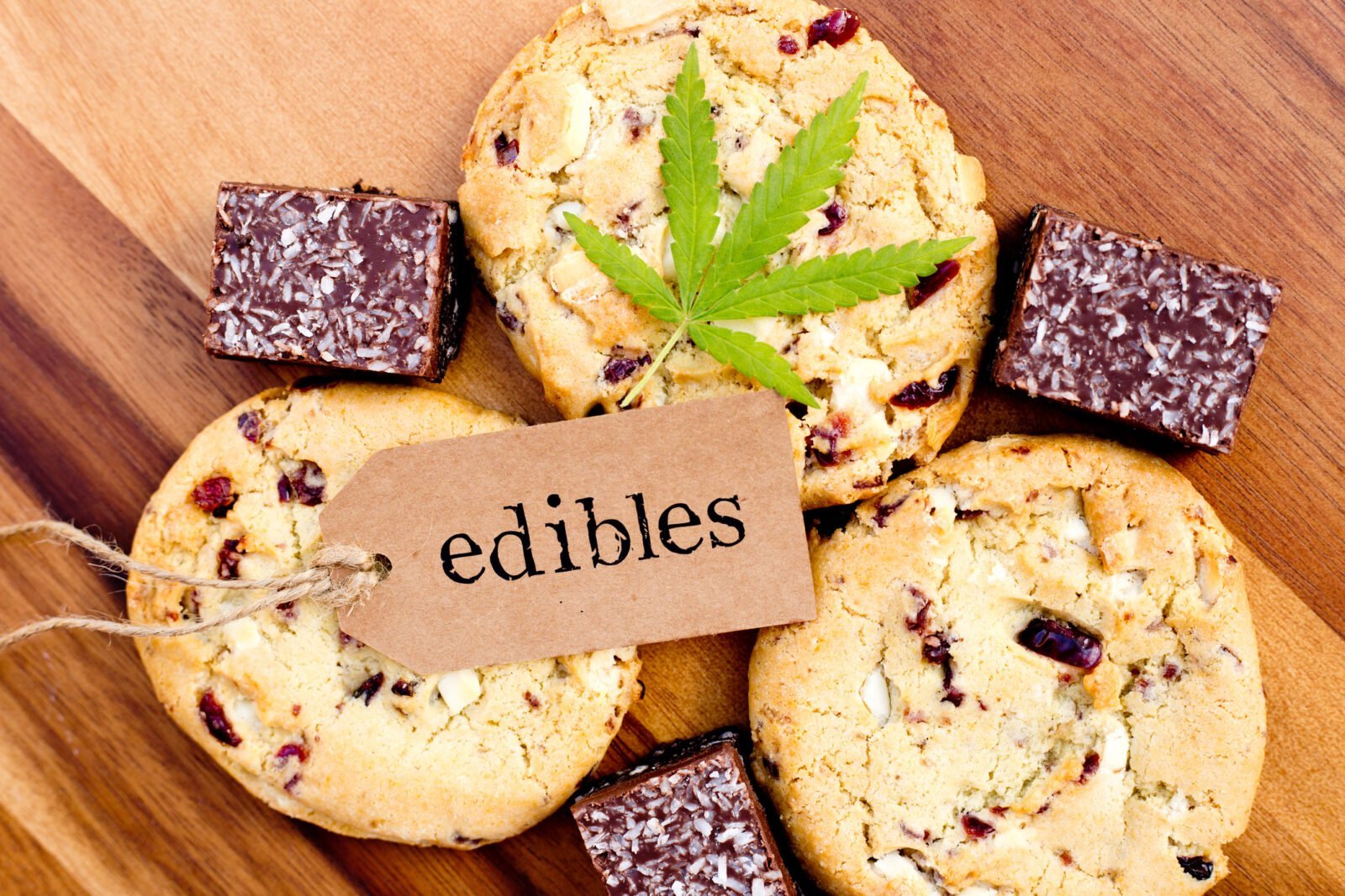 Es sind Kekse, und Brownies zu sehen auf denen ein Cannabisblatt liegt. Darauf liegt ein Schild auf dem Edibles steht.