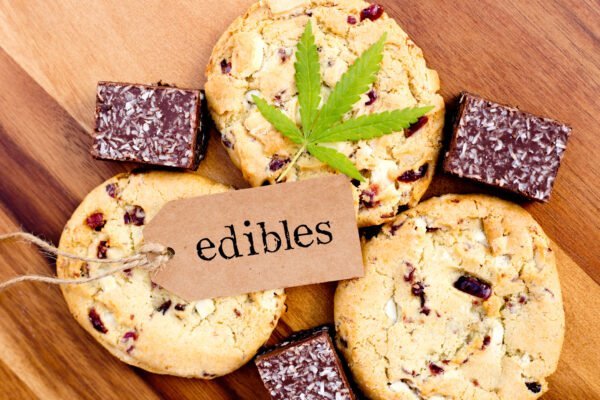 Es sind Kekse, und Brownies zu sehen auf denen ein Cannabisblatt liegt. Darauf liegt ein Schild auf dem Edibles steht.