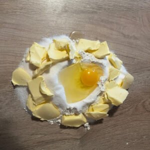 Hier ist ein Haufen Mehr zu sehen, mit Butterstückchen, einem Ei und Zucker darauf. Das wird der Mürbteig für die Hanfplätzchen