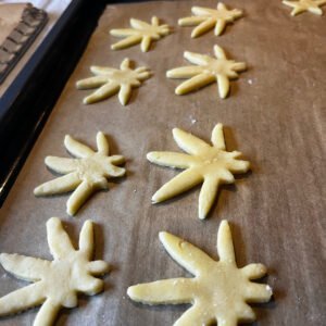 Plätzchen in Hanfform liegen auf einem Backblech mit Backpapier. 