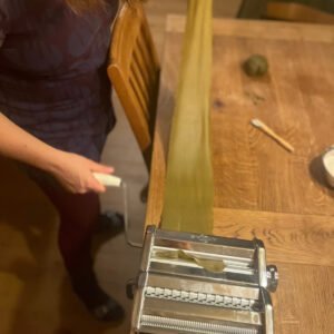 Hier sieht man eine Frau, die an einer Nudelmaschine steht, und einen langen Nudelteig duchlässt.