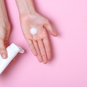 Auf einem rosa Hintergrund sieht man eine ausgestreckte Hand, auf deren Handinnenfläche ein Klecks Creme ist. Die andere Hand hält eine Cremetube. 