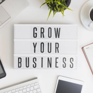 ein Schreibtisch ist von oben zu sehen, darauf liegt ein eine Tastatur, ein Tablet, ein Blog eine Kaffeetasse und eine Pflanze. Das Bild ist von oben aufgenommen und in der Mitte ist ein Schild auf dem steht: grow your business