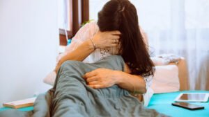 eine Frau ist zu sehen, die im Bett sitzt und sich den Kopf hält.