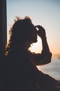 Eine Frau sitzt auf gegen das Licht und hält sich den Kopf.