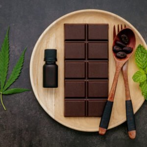 Eine Tafel Schokolade mit einem Minzblatt, einem Cannabisblatt und einem Ölfläschchen auf einem Holzteller