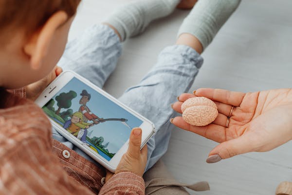Hier sitzt ein Kind das ein Handy auf dem Schoss hat und Medien konsumiert. Zu viele Medien können zu einem Dopamin Überschuss führen.