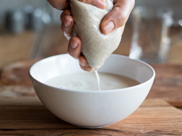 Durch einen Nussmilchbeutel wird in eine Schale eine Milchalternative gewonnen.