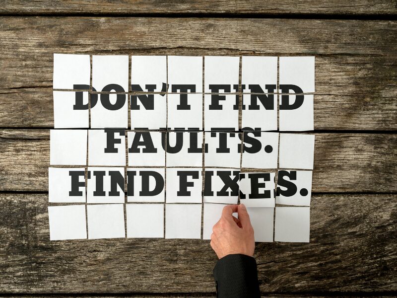 Eine Hand hält ein Blatt Papier mit schwarzem Text: dont find faults, find fixes.
