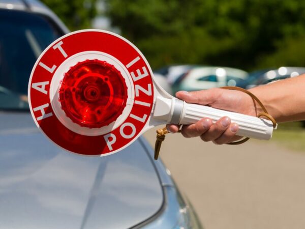 Eine Polizeikelle ist zu sehen. Ein Auto wird aufgehalten