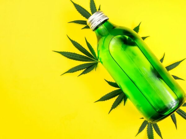 THC Getränk - eine Flasche mit Cannabisblättern vor gelbem Hintergrund