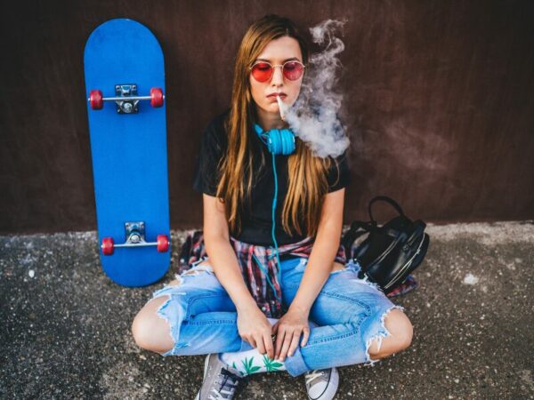 Prävention bei Jugendlichen! Ist diese zeitgemäßg und ausreichend? Ein junges Mädchen zieht an einem Joint, mit blauen Kopfhörern, einem blauen Skateboard und einer orangenen Sonnenbrille.
